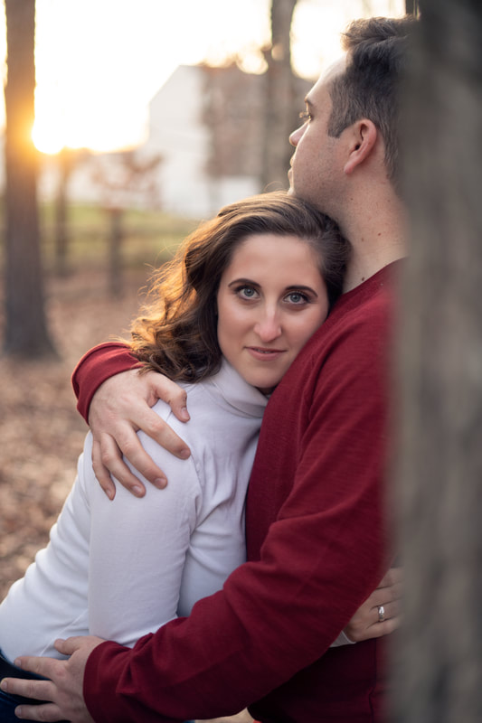 Bride to be looking directly at camera hugging fiance during fall